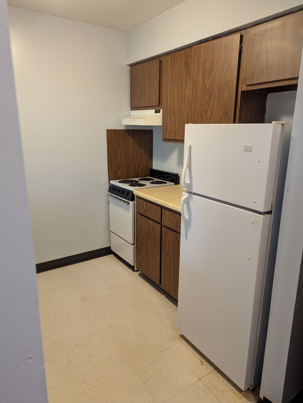 A white refrigerator stands in a kitchen with wooden cabinets.