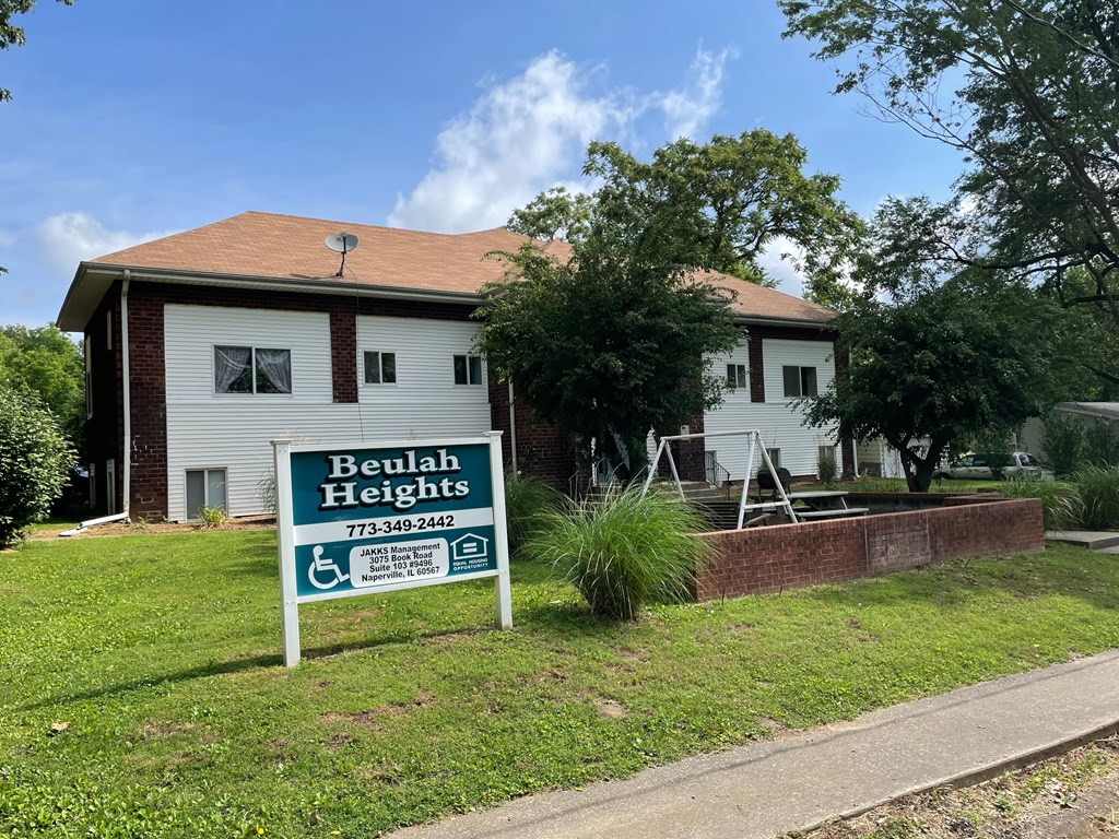 A sign for Beulah Heights is in front of a brick house.