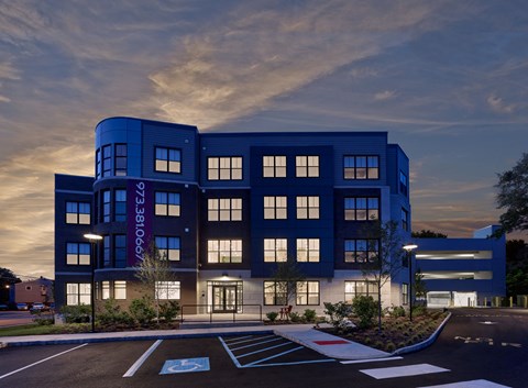 A modern building with a blue facade and a parking lot in front.