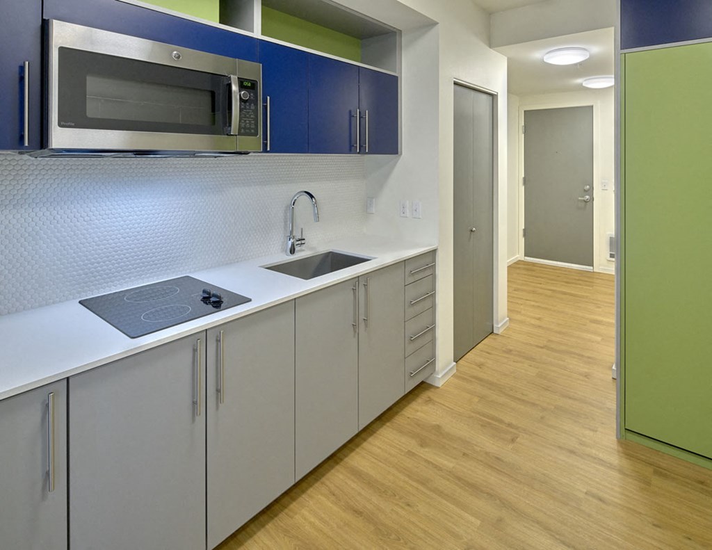 a kitchen with a sink and a microwave   and a hallway with a door