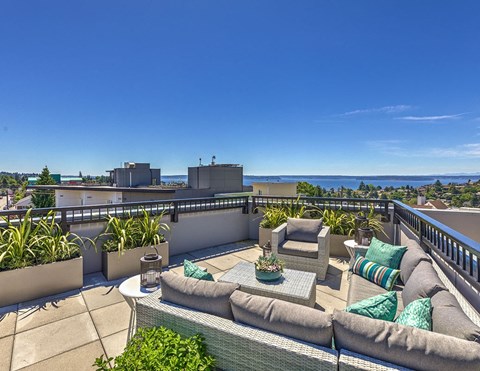 a rooftop patio with couches and a view of the city and the ocean