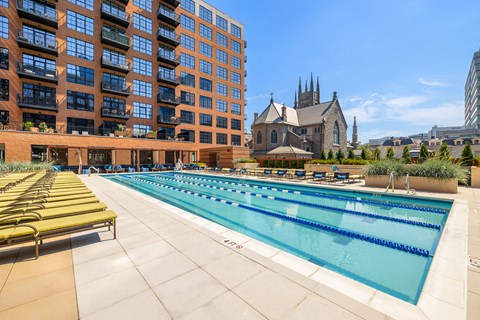 A large swimming pool with lounge chairs is surrounded by a building.