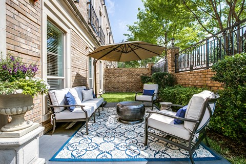 A patio with a white couch, a blue rug, and a brown umbrella.