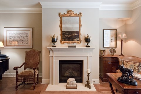 A room with a fireplace, a chair, a table, and a painting on the wall.
