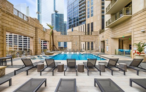 A pool surrounded by lounge chairs in a courtyard.
