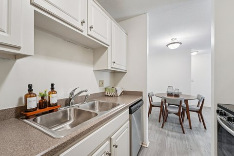 A kitchen with a sink, dishwasher, and a table with chairs.