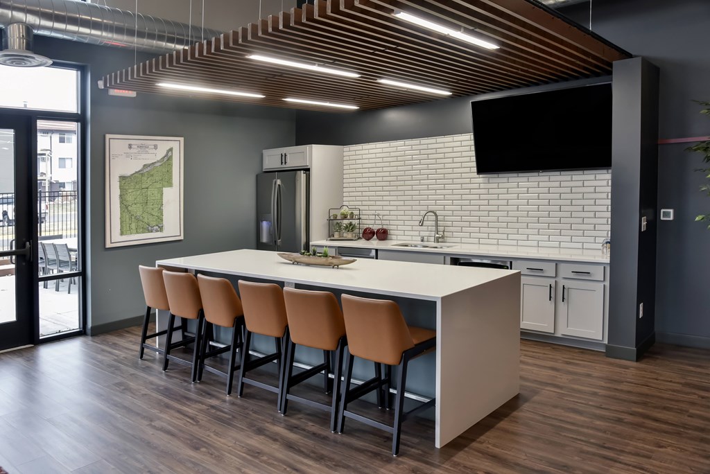 A modern kitchen with a long white island and brown chairs.