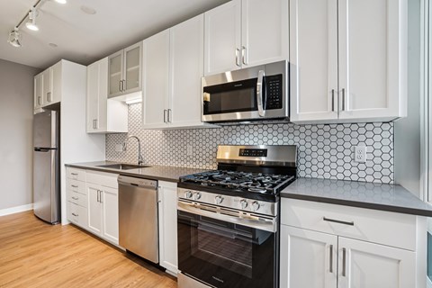 A kitchen with white cabinets and a black and white tiled backsplash.