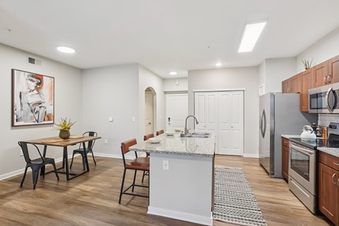 A kitchen with a table and chairs in the foreground and a refrigerator, microwave, and oven in the background.