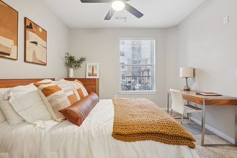 A bedroom with a bed, desk, and window.