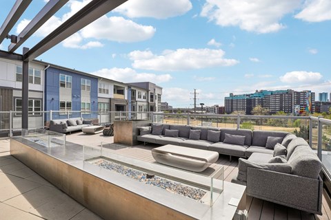 A modern outdoor seating area with a glass table and grey couches.