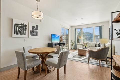 A modern dining room with a round wooden table and grey chairs.