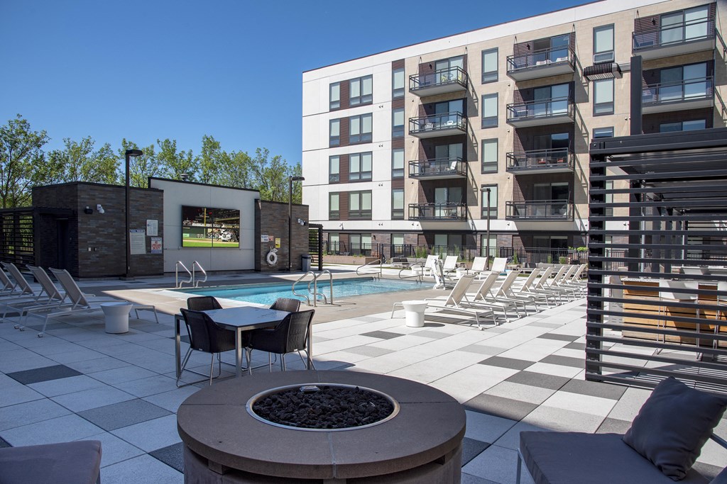 Resort style pool area with deck, grilling area, fire pit, and large mounted TV near pool.