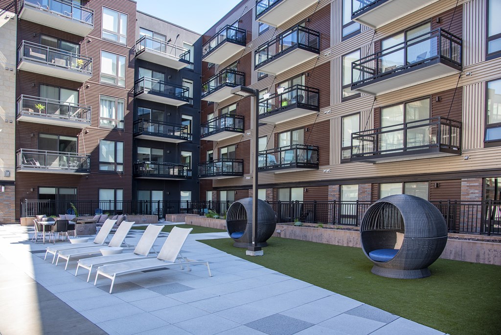 Pool deck furnished with lounge chairs and green space against the background of apartment balconies.