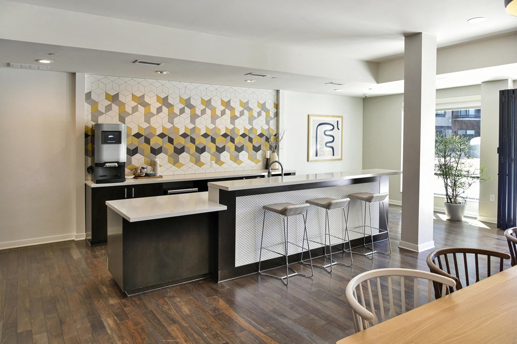 24/7 Coffee bar in naturally lit community space against a yellow geometric accent wall.