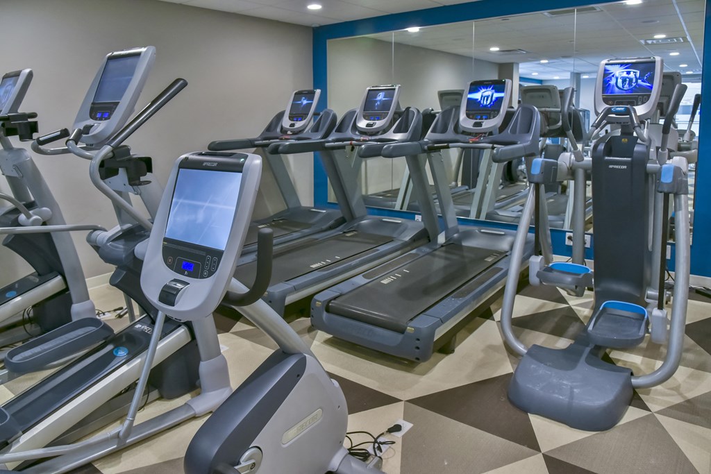 24 hour fitness center equipped with treadmills and a variety of cardio machines against a mirrored wall.