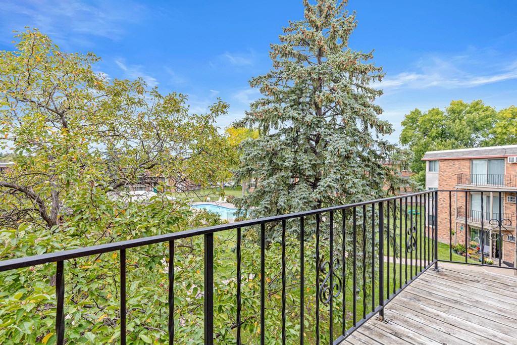 A balcony with a black railing overlooks a pool and trees.