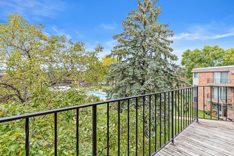 A balcony with a black railing overlooks a pool and trees.