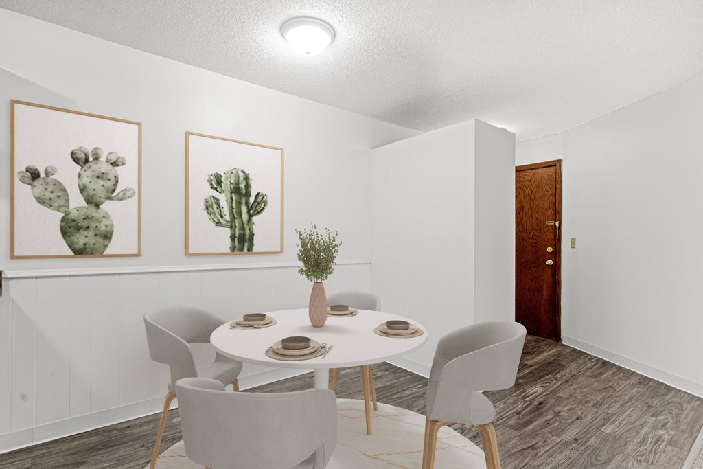 A dining room with a table set for two and two cactus pictures on the wall.