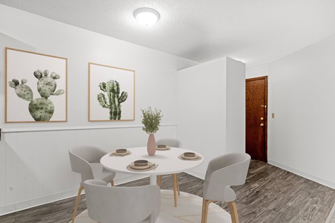 A dining room with a table set for two and two cactus pictures on the wall.