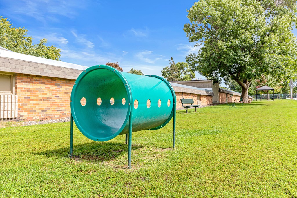 A green tube slide in a grassy area with a building in the background.