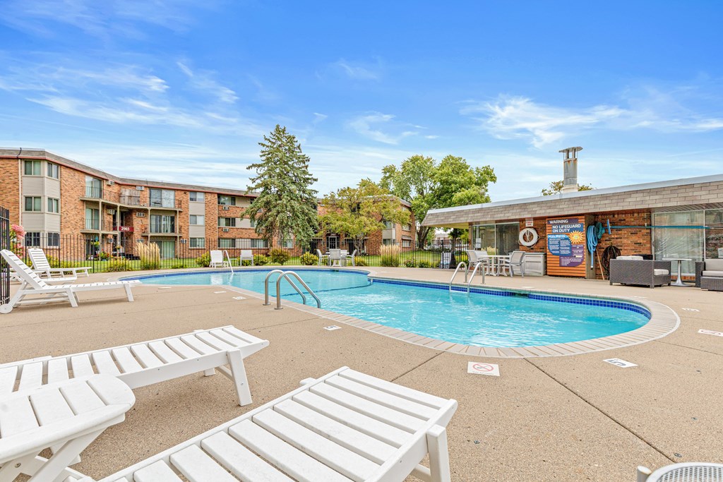 A pool area with sun loungers and a building in the background.