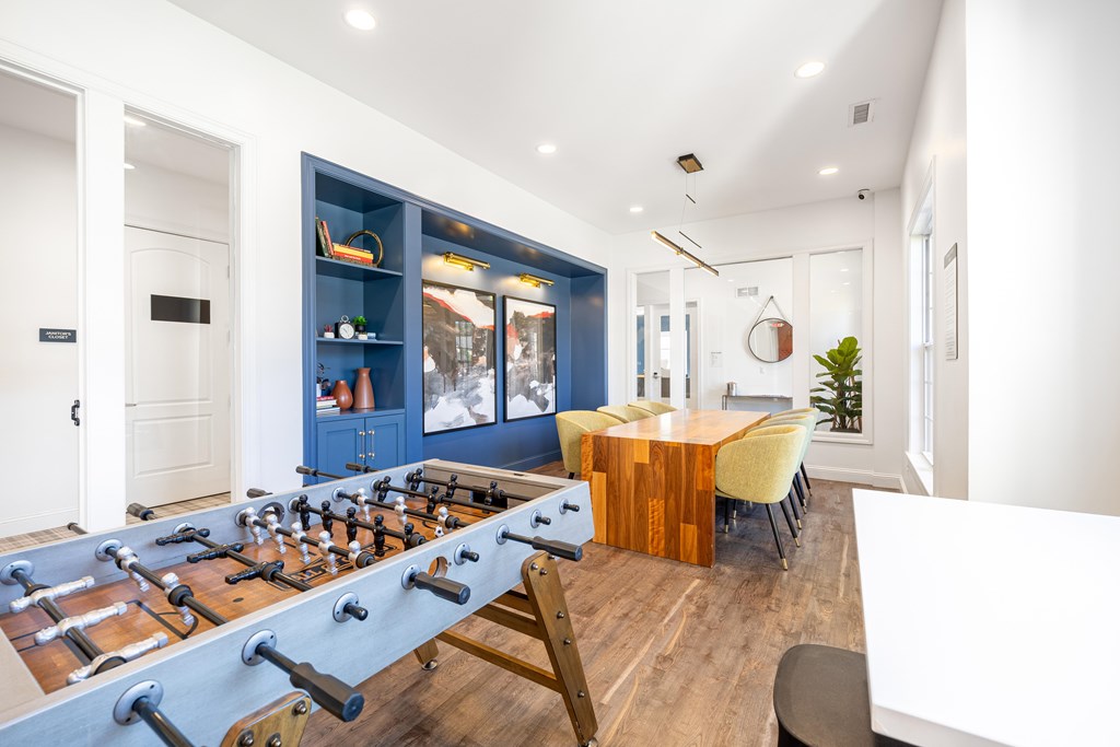 A foosball table is in the middle of a room with a blue cabinet and a wooden table.
