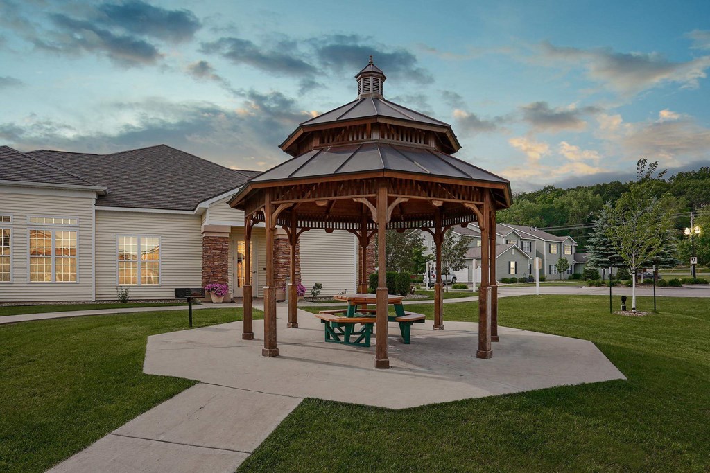 Private gazebo surrounded by lush green lawn with walkway leading to building.