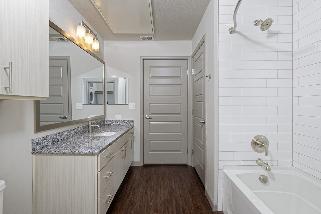 Bathroom with wood floor, granite sink countertop and bathtub with white tiles