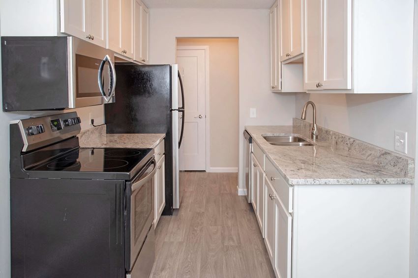 Modern kitchen with white cabinetry, stainless steel appliances, and vinyl wood style flooring throughout kitchen into the dining room.