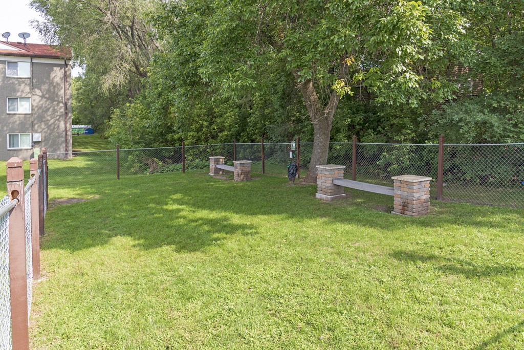 A green grassy area with a fence and a tree.