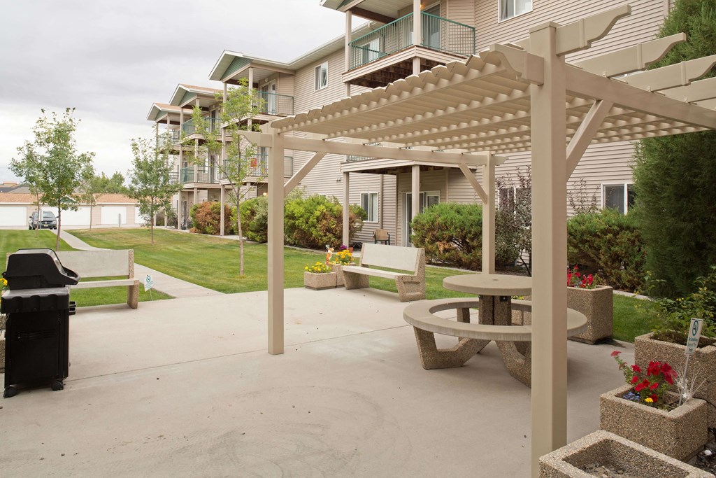 Outdoor grilling area with picnic tables and seating all under a shaded pergola.