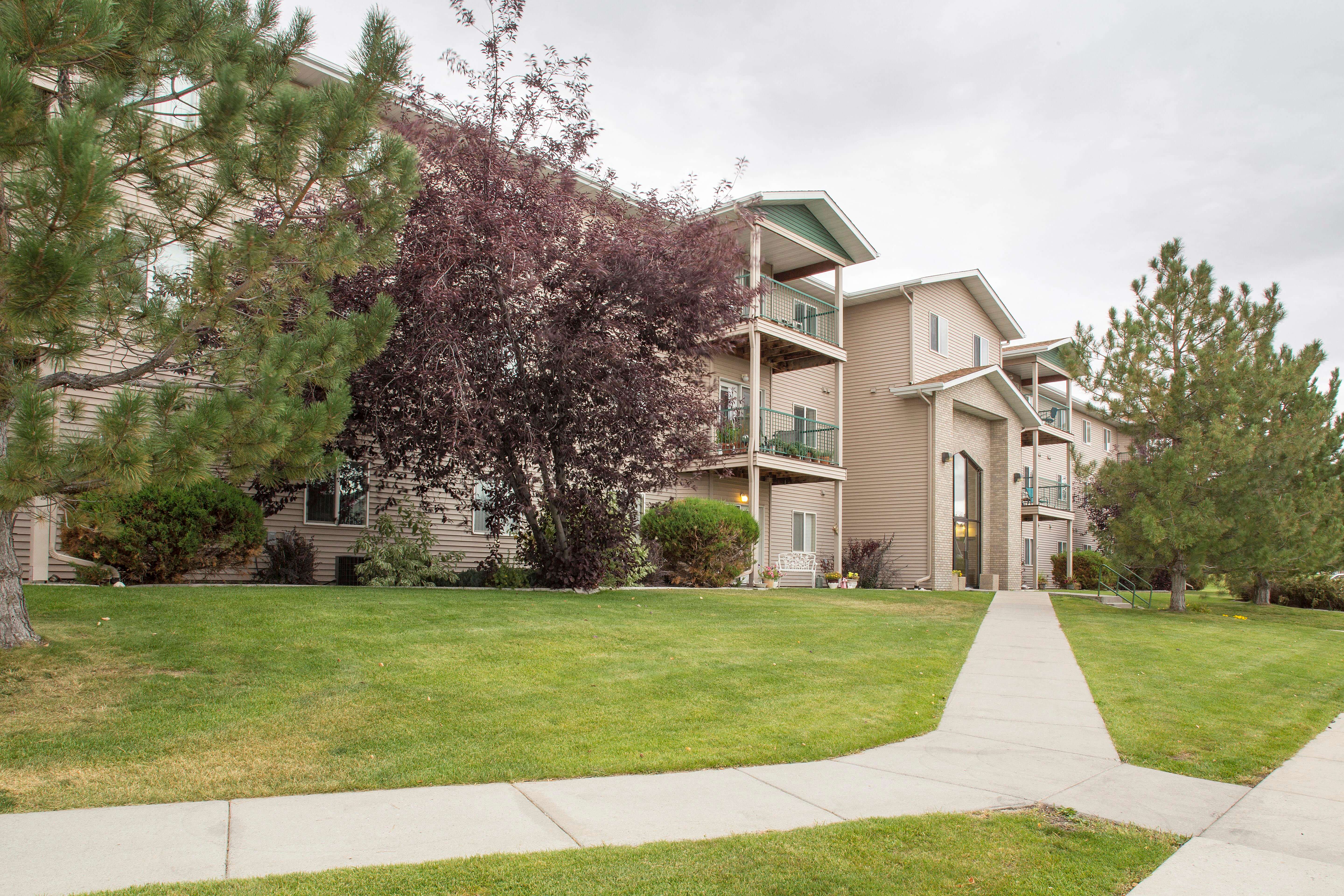Building exterior of Country Meadows with lush green grass and sidewalks leading up to the building entrance.