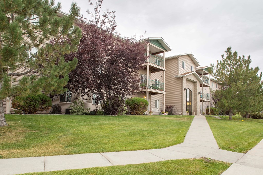 Building exterior of Country Meadows with lush green grass and sidewalks leading up to the building entrance.