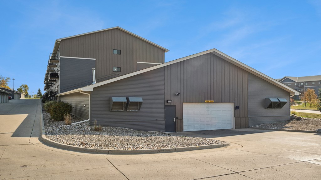 A large metal building with a garage door and a small tree in front.