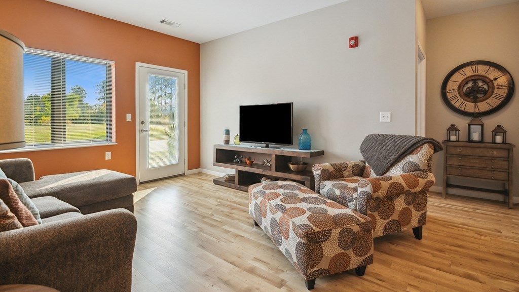 A living room with a grey couch, a brown patterned ottoman, and a flat screen TV.