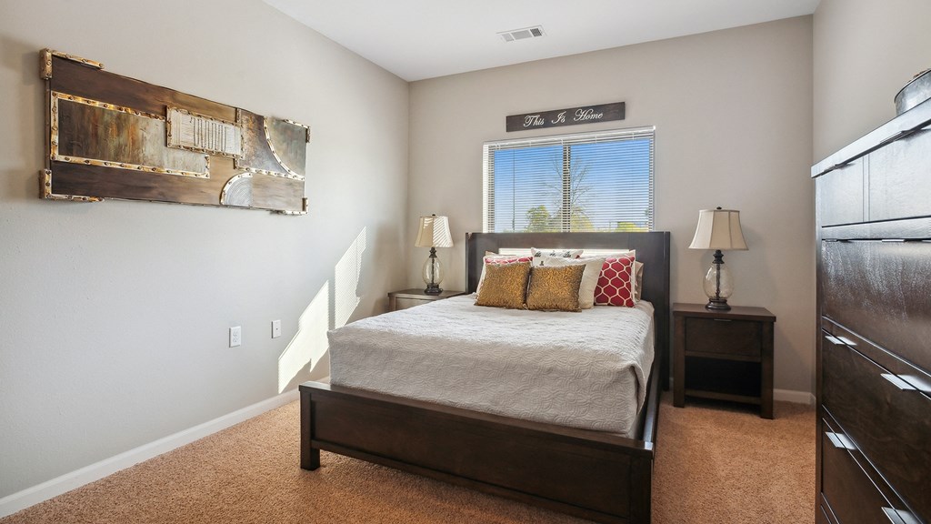 A bedroom with a bed, two lamps, and a painting on the wall.