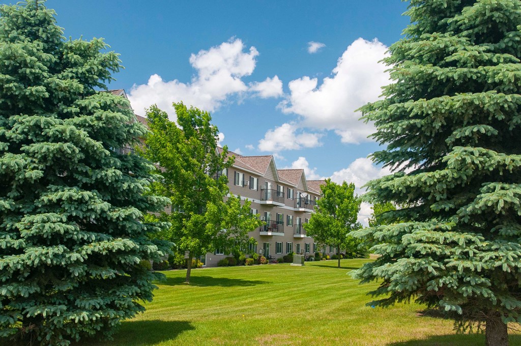 Evergreen Apartments building nestled between some trees against a blue sky.