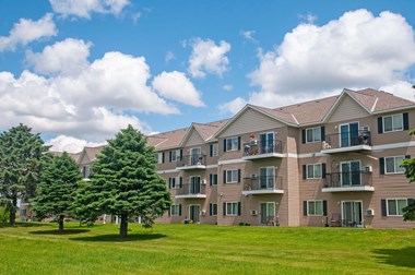 Full building exterior of Evergreen Apartments on a lush green lawn and evergreen trees on the left side.