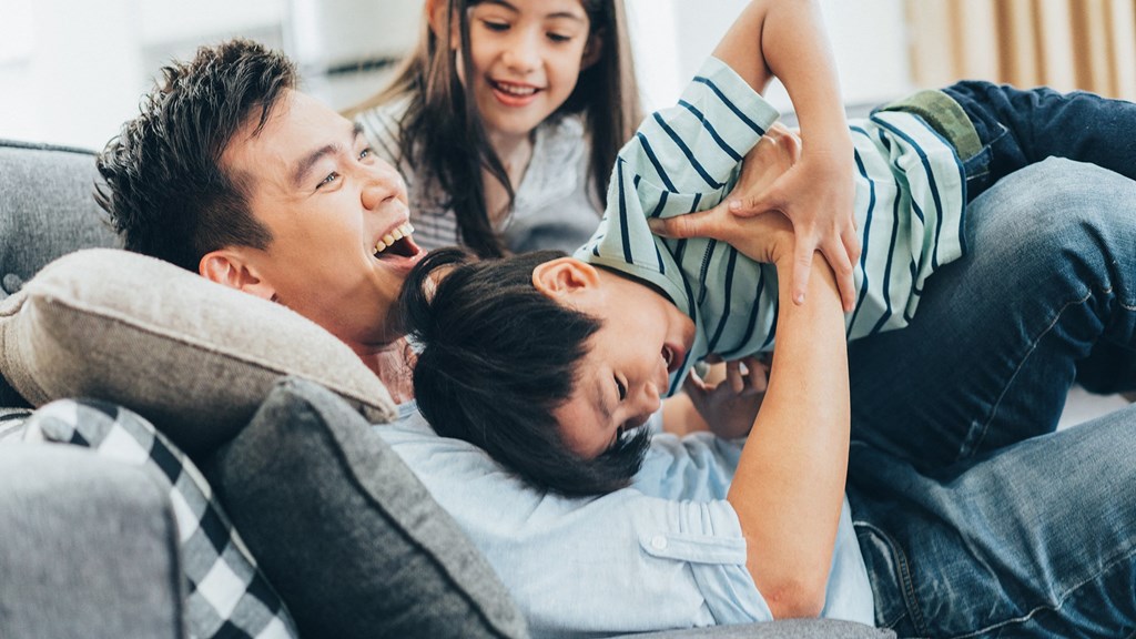 a father plays with his son and daughter on the couch