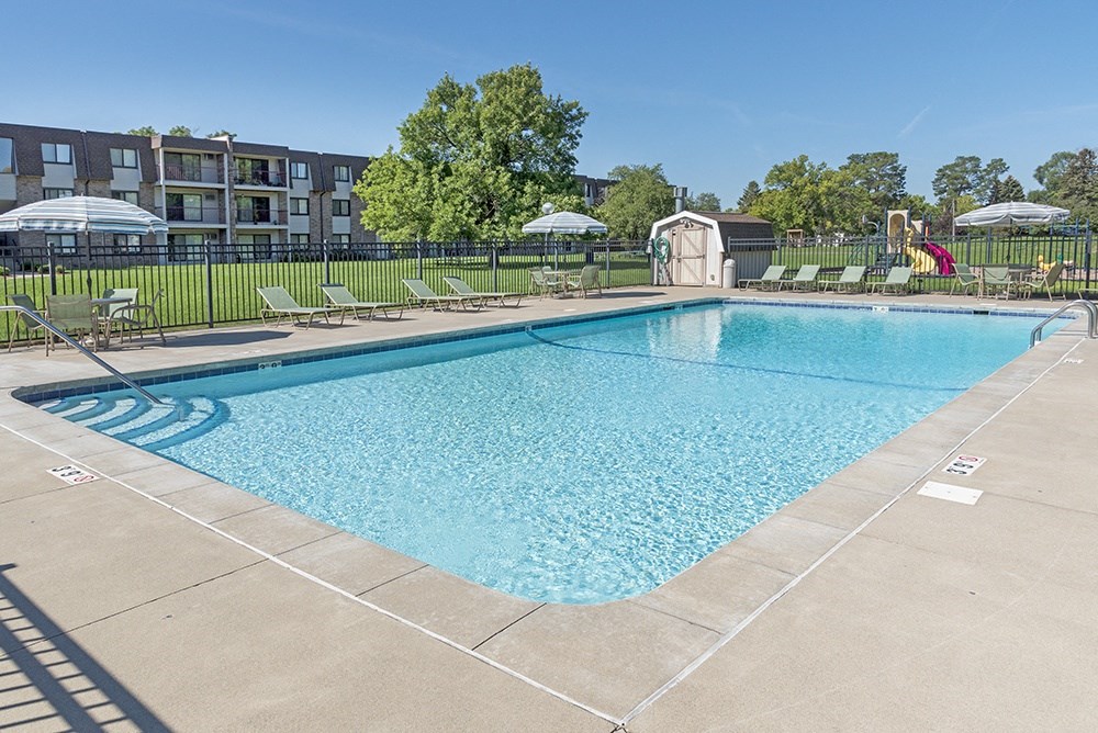 a swimming pool with chairs and umbrellas and a building in the background