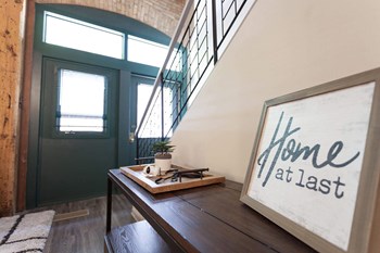 Entryway of unit with iron staircase leading up and black double doors with glass inserts opposite the stairs. Sign on console table by staircase reads