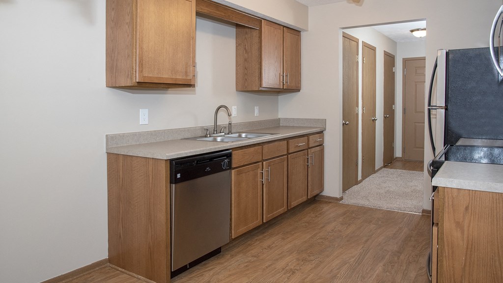an empty kitchen with wooden cabinets and a stainless steel dishwasher