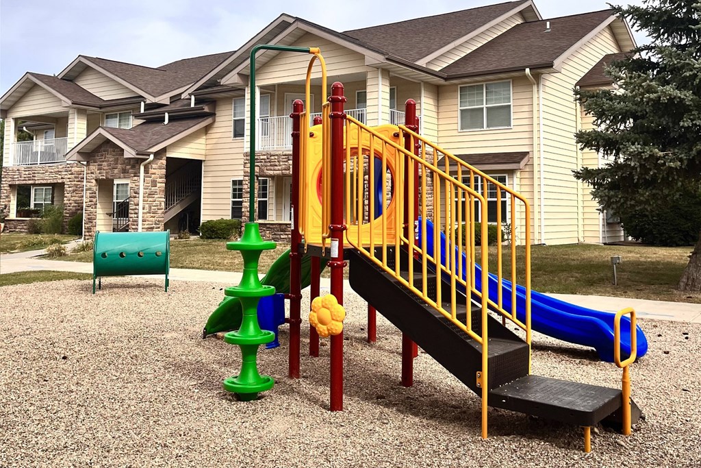 a playground with a slide and climbing equipment in front of a yellow house