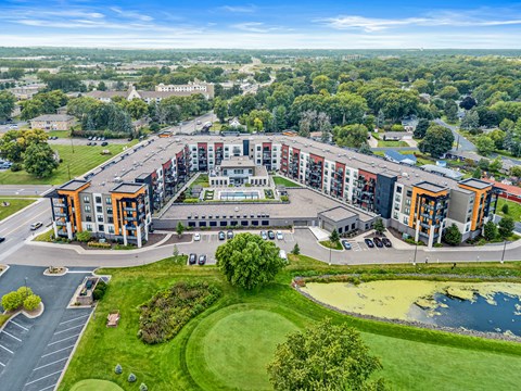 A large, multi-story building with a parking lot in front and a pond in the front yard.