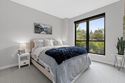 A bedroom with a large bed and a window overlooking a tree-filled landscape.