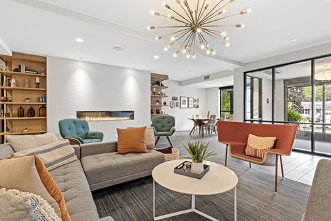 A living room with a grey sofa, a green armchair, a brown armchair, a white coffee table, a fireplace, and a chandelier.