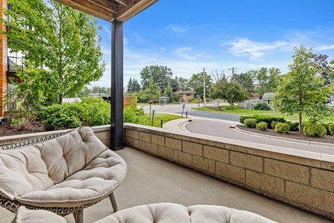 A patio with a cushioned chair and a table is overlooking a street.