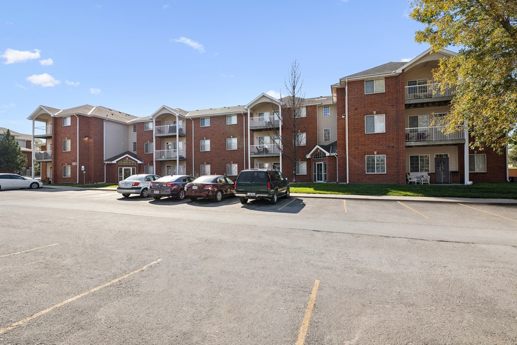 A parking lot in front of a red brick apartment building with cars parked.