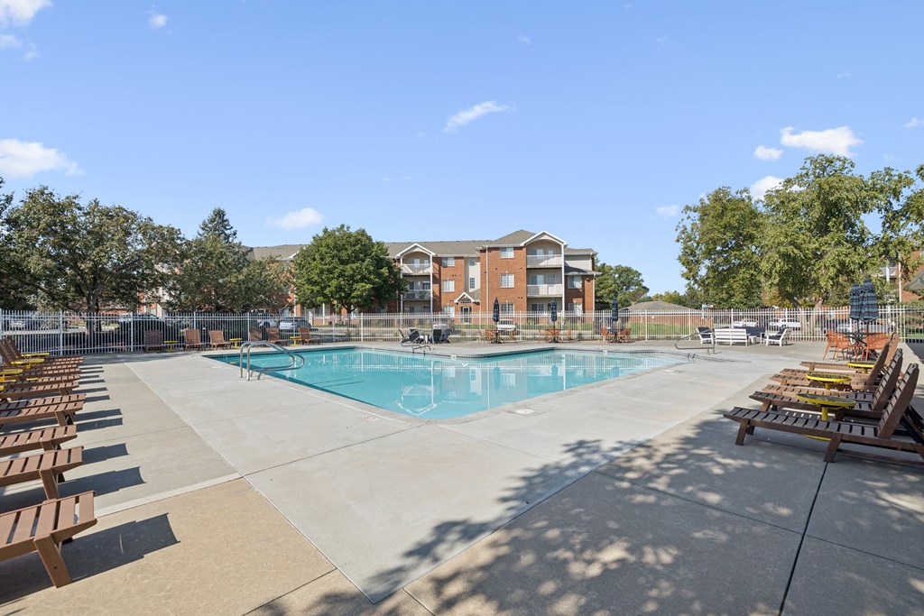 A large swimming pool surrounded by sun loungers and trees.